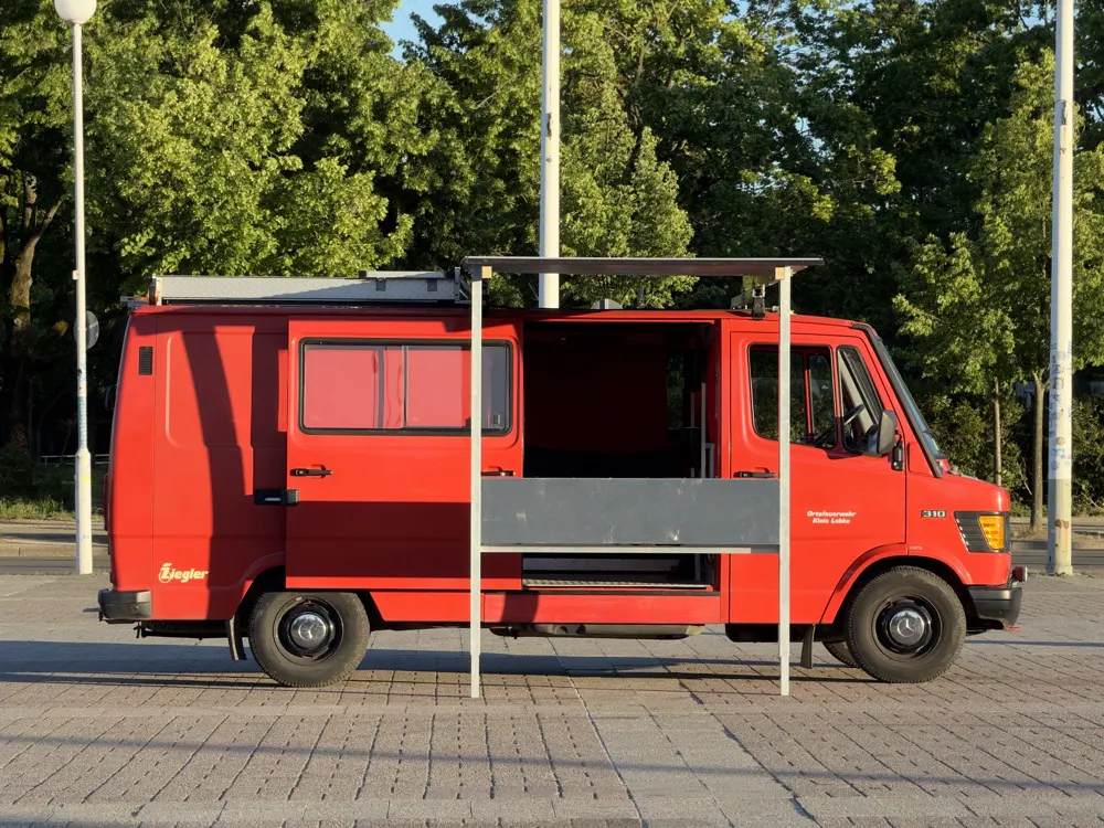Der Bombero-Wagen von der Seite vor grünen Bäumen
